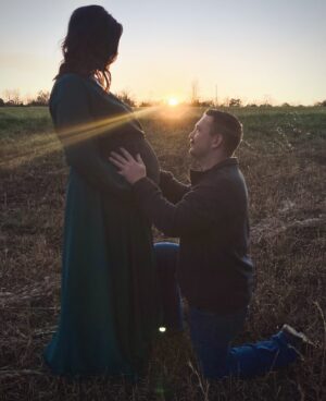 Tyler kneeling in a field with his hands on Adrienne’s belly pregnant with their rainbow baby Henry | Tennessee Reproductive Medicine, Chattanooga, TN