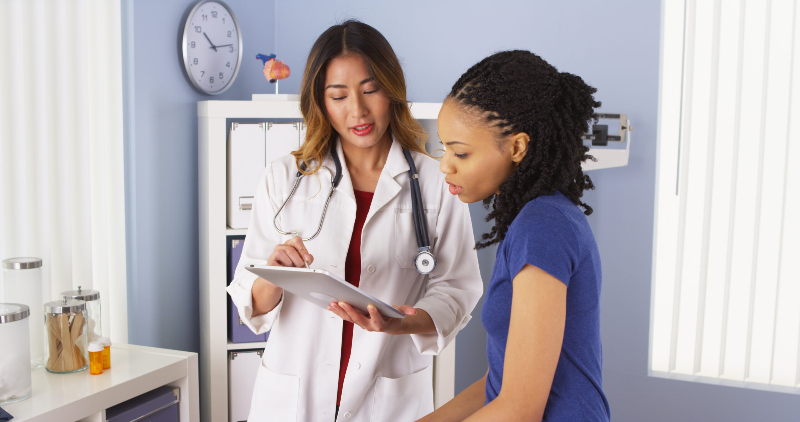 Asian doctor explaining ovarian cyst issues to African American female patient using tablet