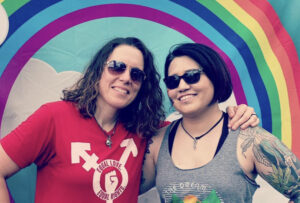 Jessica and Jennifer both wearing dark glasses and standing in front of a rainbow image, grew their LGBT family with the help of Tennessee Reproductive Medicine and embryo donors | Chattanooga, TN